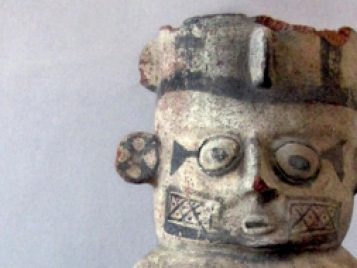 Painted earthenware vase with a person's face, wearing headwear, and large earrings pointing outward.